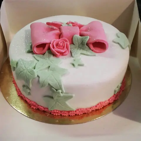 Gâteau blanc décoré d'un grand nœud rose et de feuilles de lierre en pâte à sucre