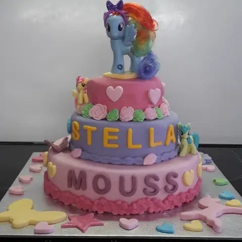 Gâteau à trois étages rose et violet, surmonté d'une figurine de poney à crinière arc-en-ciel