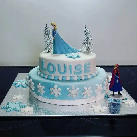 Gâteau bleu clair à deux étages, flocons blancs et figurines de la Reine des neiges