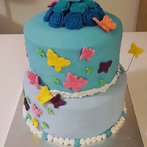 Gâteau bleu à deux étages couvert de papillons multicolores, roses bleues au sommet