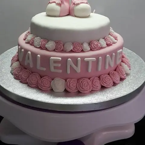 Gâteau rose à deux étages bordé de roses, avec des chaussons de bébé au sommet