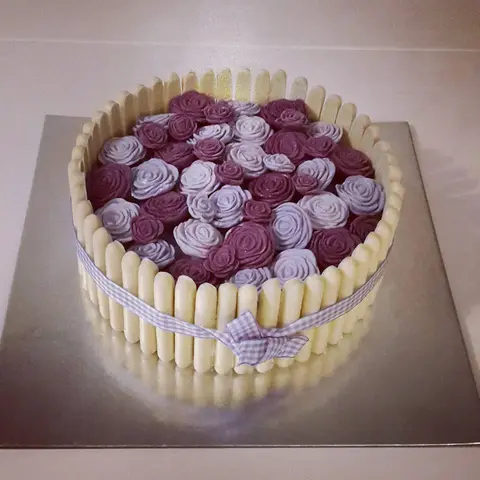 Charlotte entourée de biscuits blancs et d'un ruban vichy, couverte de roses violettes en crème