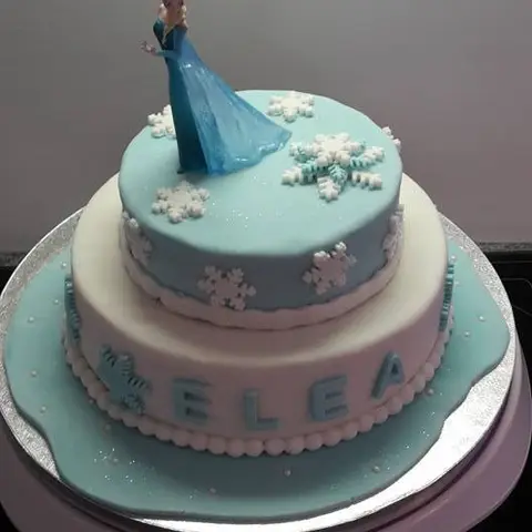 Gâteau bleu et blanc à deux étages avec une figurine de la Reine des neiges et des flocons