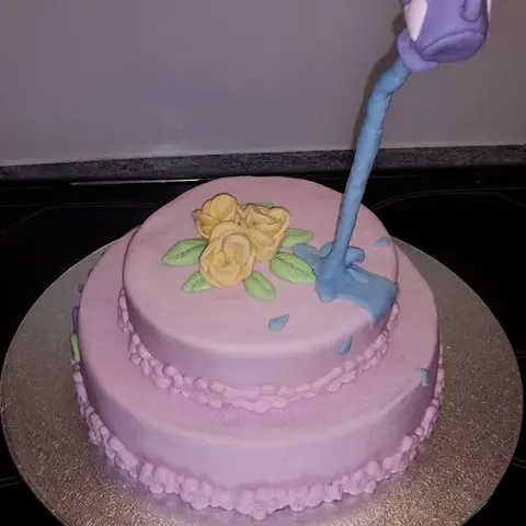 Gâteau rose à deux étages, un arrosoir violet suspendu qui verse de l'eau en sucre sur des roses jaunes