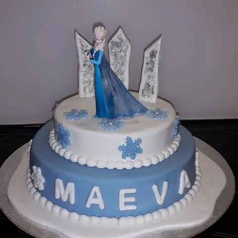 Gâteau bleu et blanc à deux étages, figurine de la Reine des neiges devant un palais de glace