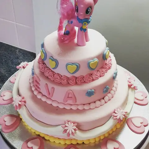 Gâteau rose à trois étages décoré de cœurs, surmonté d'une figurine de Pinkie Pie, de Mon petit poney