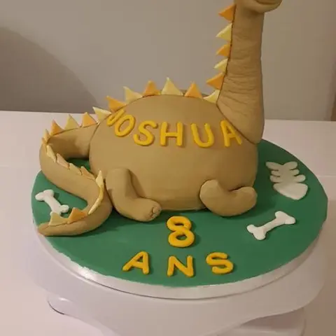 Gâteau en forme de dinosaure beige à long cou, posé sur un socle vert