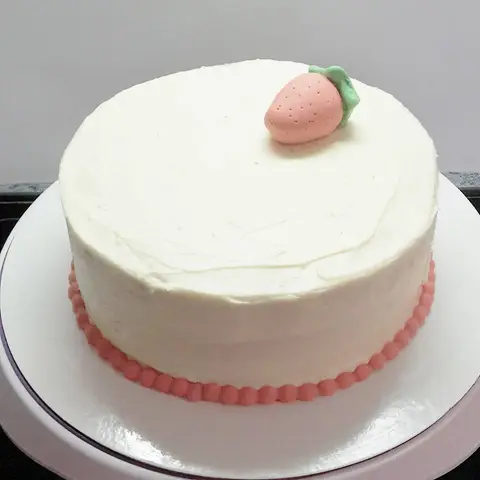 Gâteau blanc à la crème, une fraise en pâte d'amande au centre et une bordure de perles roses