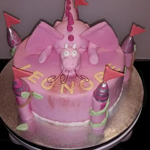 Gâteau en forme de château rose avec un dragon rose au centre et des tours à fanions