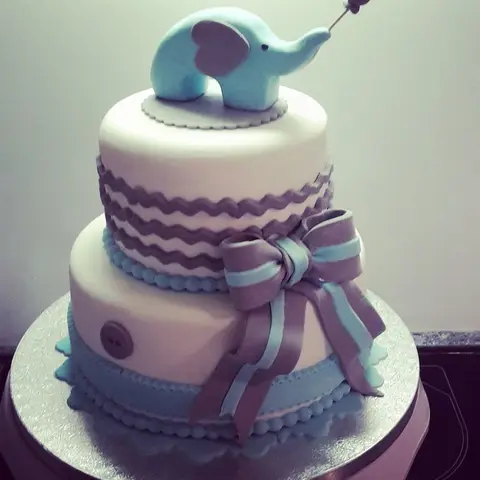 Gâteau blanc et lilas à deux étages avec un grand nœud et un éléphant bleu au sommet