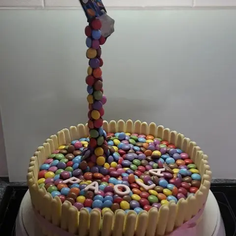 Gâteau entouré de biscuits blancs, couvert de bonbons colorés qui tombent d'un sachet suspendu