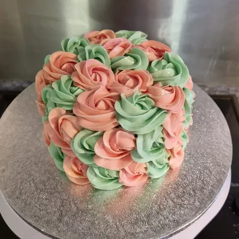 Gâteau couvert de rosaces de crème pêche et vert menthe