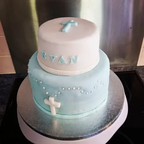 Gâteau blanc et bleu ciel à deux étages décoré de croix et de perles