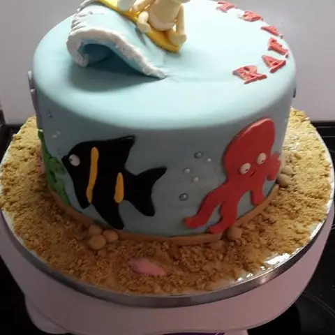 Gâteau bleu posé sur du sable en biscuit, avec un poisson noir, une pieuvre rouge et une vague