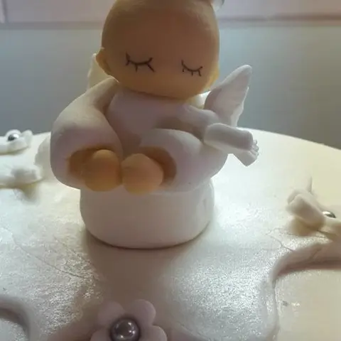 Figurine de bébé ange endormi, ailes blanches, posée sur un gâteau blanc