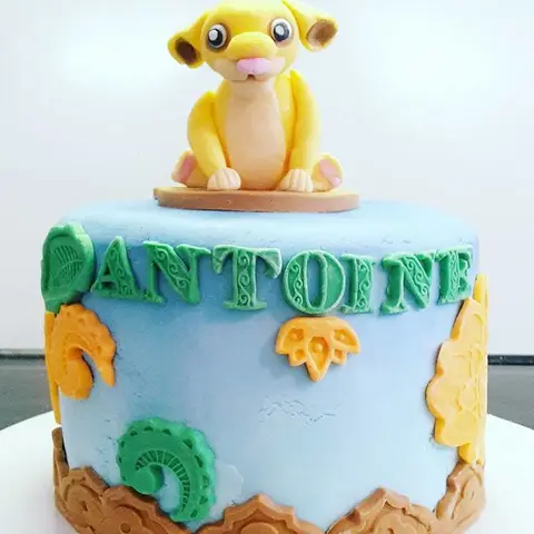 Gâteau bleu ciel surmonté d'un Simba, le lionceau jaune assis, décor de feuillages