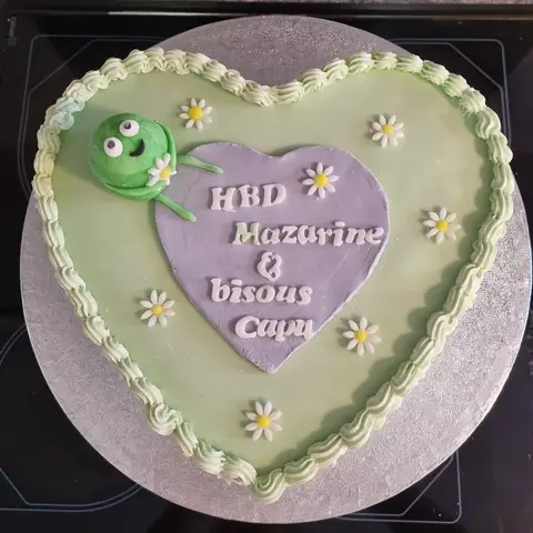 Gâteau en forme de cœur vert pâle avec une petite créature verte et des marguerites