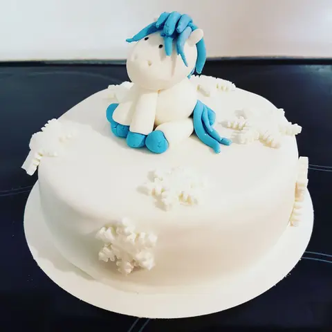 Gâteau blanc à flocons surmonté d'un poney blanc à crinière bleue