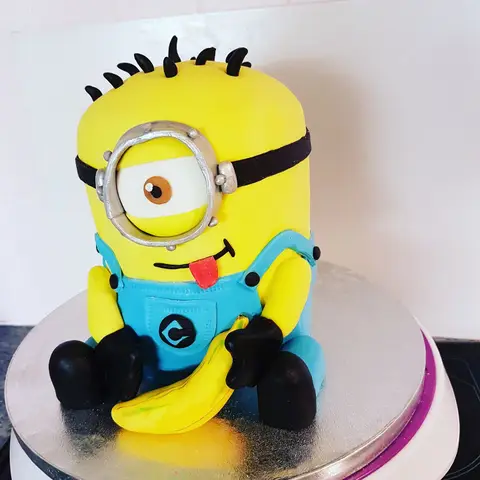 Gâteau en forme de Minion jaune en salopette bleue, tenant une banane