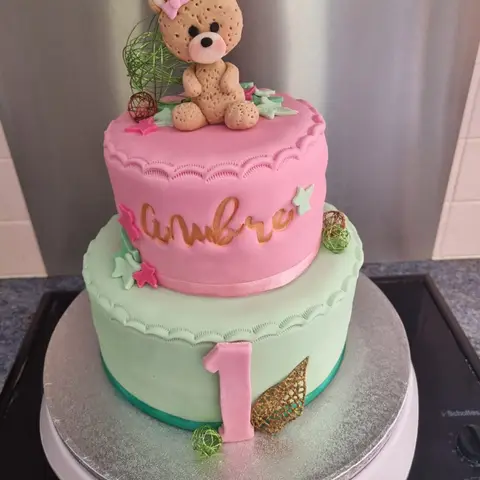 Gâteau rose et vert d'eau à deux étages avec un ourson au sommet et le chiffre 1