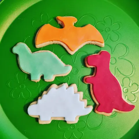 Quatre sablés en forme de dinosaures, orange, vert, blanc et rose