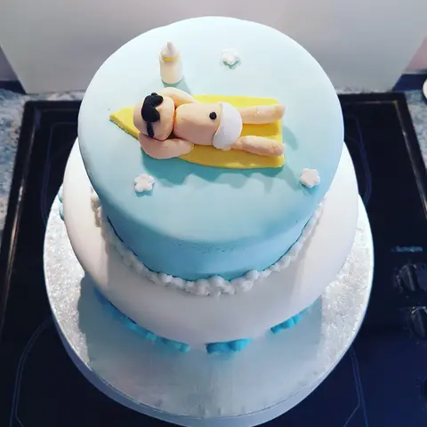 Gâteau bleu et blanc à deux étages avec un bébé allongé sur une serviette jaune