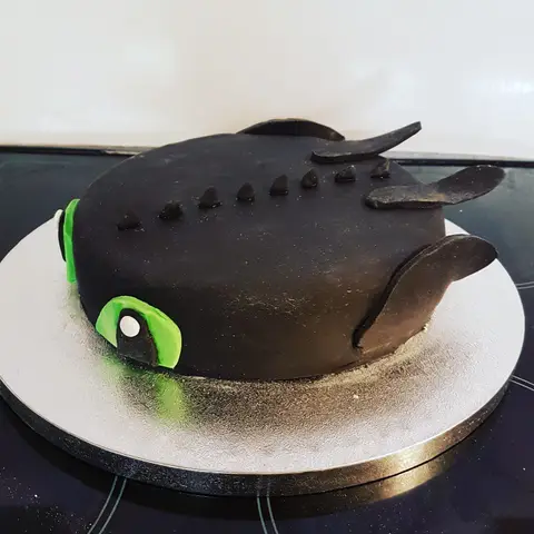 Gâteau en forme de Krokmou, le dragon noir aux yeux verts, ailes repliées