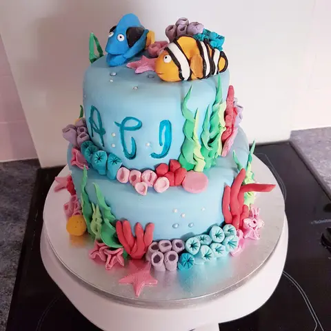 Gâteau bleu à deux étages couvert de coraux, avec un poisson-clown et un poisson bleu