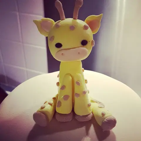 Figurine de girafe jaune à taches violettes, assise sur un gâteau
