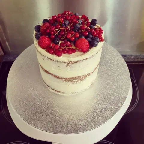 Naked cake à trois couches surmonté de fraises, de groseilles et de myrtilles