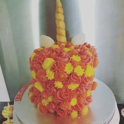 Gâteau licorne couvert de rosaces orange et jaunes, avec une corne dorée