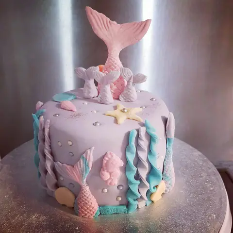 Gâteau lilas décoré de queues de sirène roses, d'algues bleues, de coquillages et d'une étoile de mer