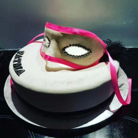 Gâteau noir et blanc surmonté d'un masque de carnaval à ruban rose