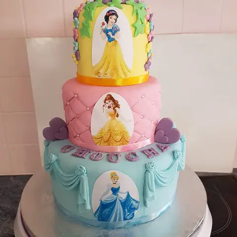 Gâteau à trois étages jaune, rose et bleu, une princesse de conte sur chaque étage