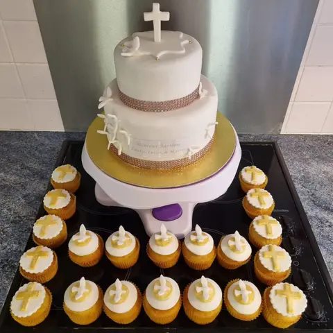 Pièce montée blanche surmontée d'une croix, entourée de cupcakes décorés de croix