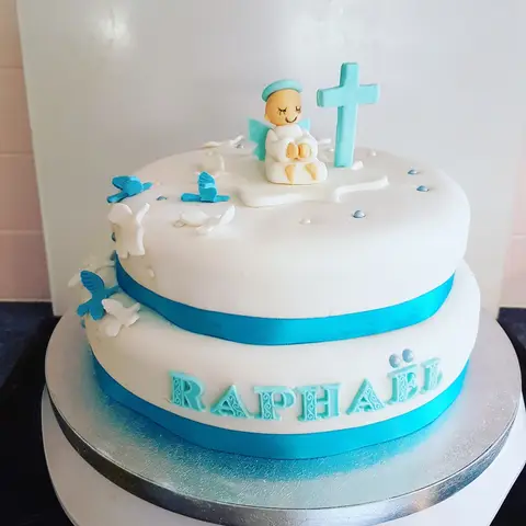 Gâteau blanc à deux étages ceint d'un ruban bleu, avec un ange et une croix bleue