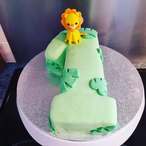 Gâteau vert en forme de chiffre 1 décoré de feuilles, un lionceau au sommet