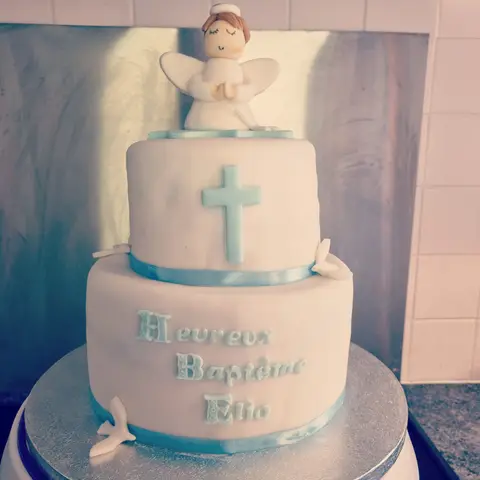 Gâteau de baptême blanc et bleu à deux étages avec une croix et un ange aux mains jointes