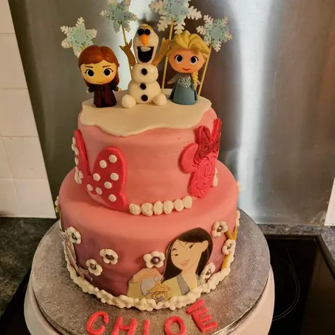 Gâteau rose à deux étages surmonté de figurines de la Reine des neiges et de flocons