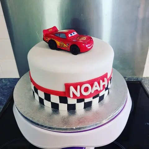 Gâteau blanc à damier noir et blanc surmonté d'une Flash McQueen, la voiture de course rouge