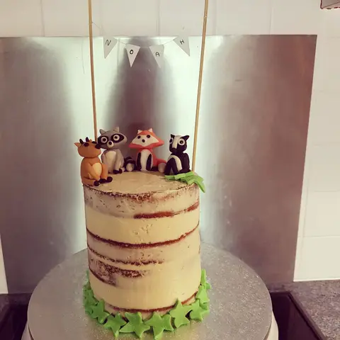 Naked cake haut surmonté d'un renard, d'un raton laveur et d'un hibou sous une guirlande