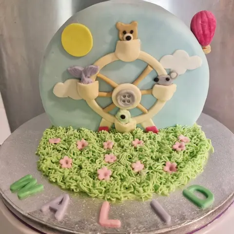 Gâteau bleu ciel avec une grande roue, un ourson, une montgolfière et une prairie en crème