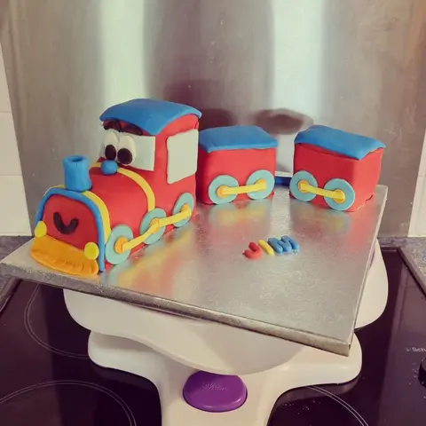 Gâteau en forme de petit train rouge et bleu avec deux wagons