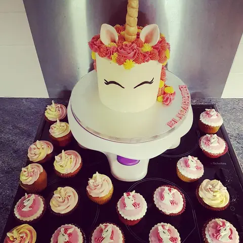Gâteau licorne blanc à crinière rose, entouré de cupcakes assortis