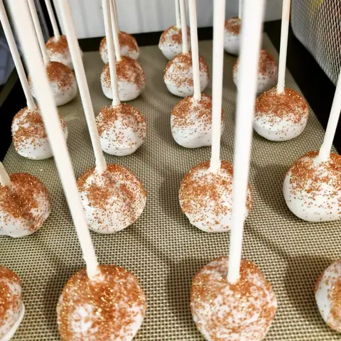 Cake pops blancs saupoudrés de paillettes dorées, piqués sur de longs bâtonnets