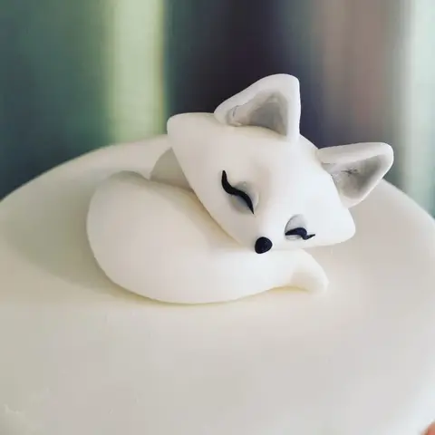 Figurine de renard polaire blanc endormi, enroulé sur un gâteau blanc