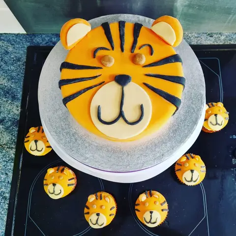Gâteau en forme de tête de tigre orange entouré de petits cupcakes tigres