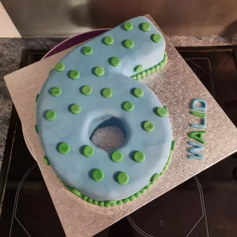 Gâteau en forme de chiffre 6 bleu ciel couvert de pois verts, avec un prénom sur le plateau