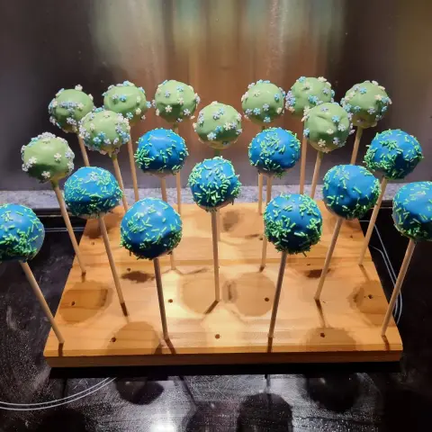 Cake pops bleus aux vermicelles verts et cake pops vert pâle aux petites fleurs, sur un support en bois