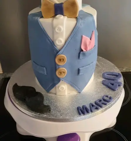 Gâteau en forme de gilet bleu sur chemise blanche, nœud papillon doré, moustache noire et chiffre 40 avec un prénom